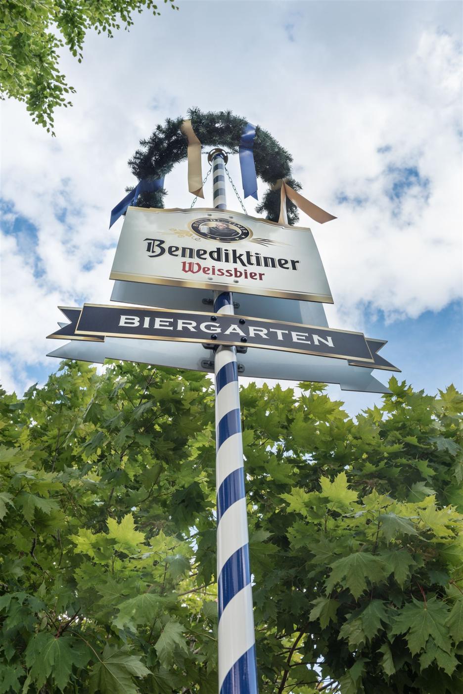 Photo shows a Bavarian maypole with a wreath at the top and below that…