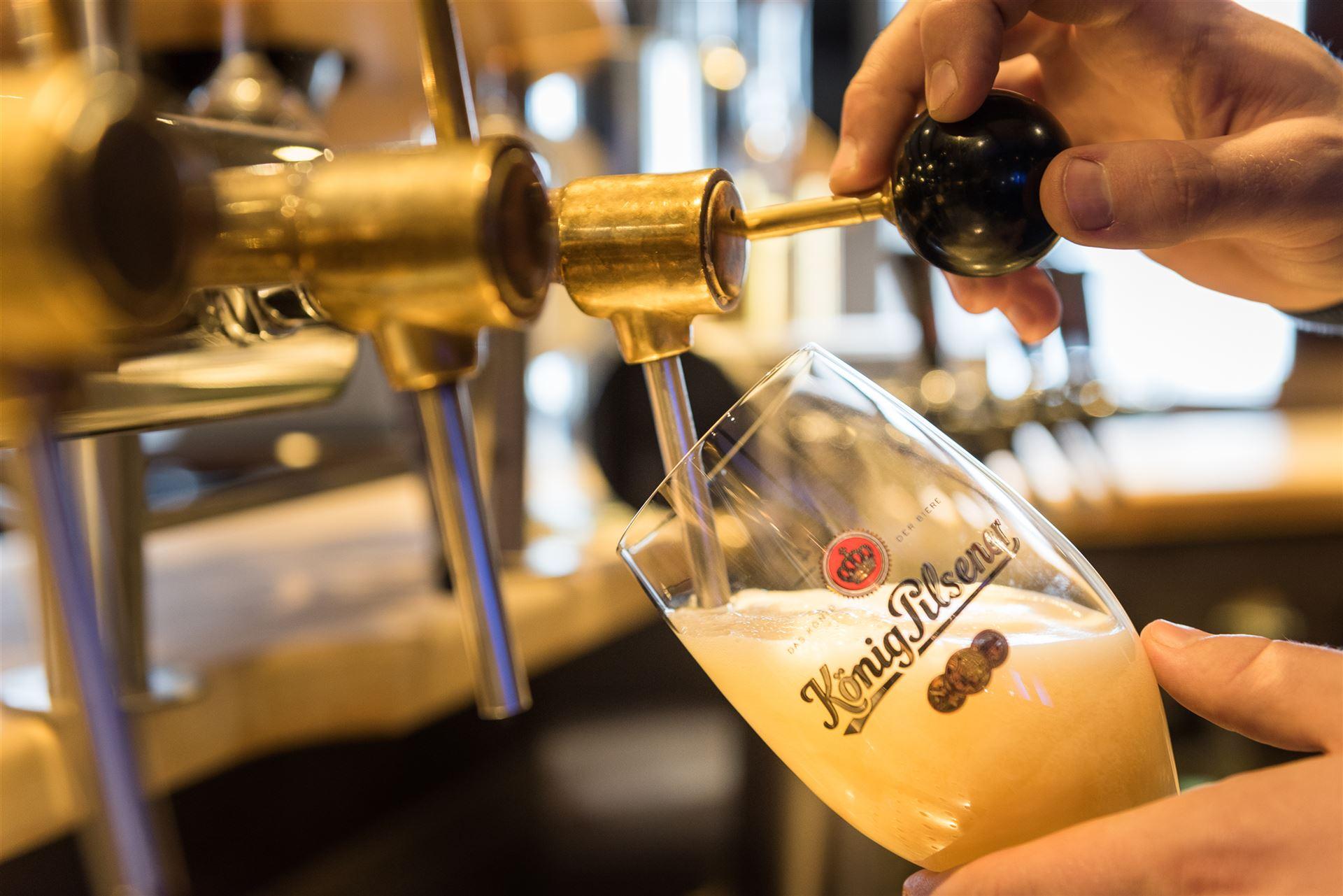 Close-up of a "König Pilsener" glass at the tap being filled with beer.