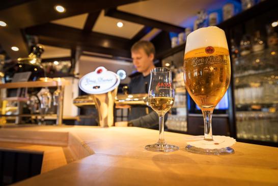 Part of the illuminated bar with, in the foreground, a glass of König Pilsener and a Sasse liqueur.
