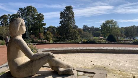 View of a seated statue in a park on a nice day.